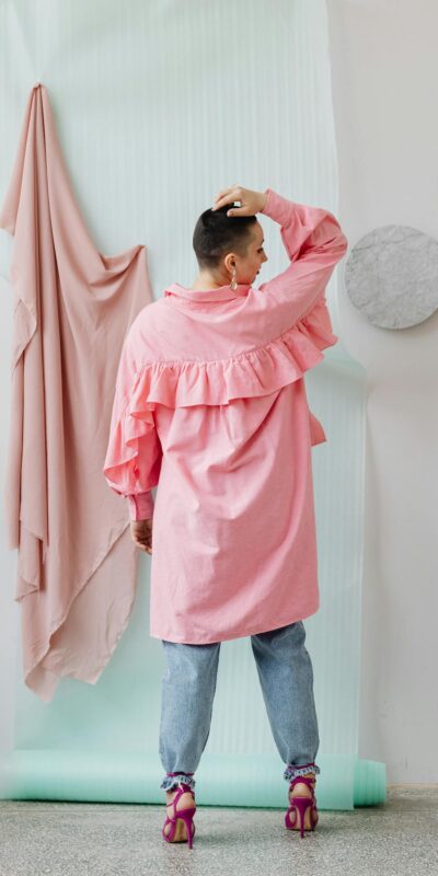 Back view of stylish woman in pink ruffled shirt and jeans, showcasing modern fashion.