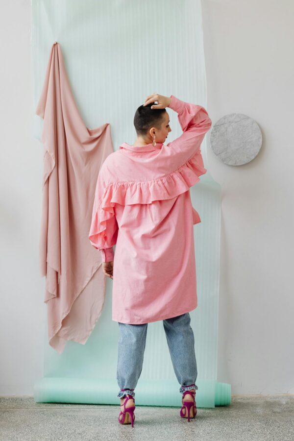 Back view of stylish woman in pink ruffled shirt and jeans, showcasing modern fashion.
