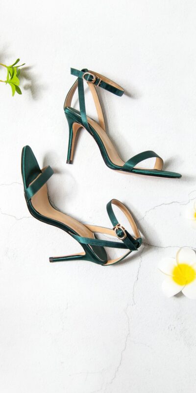 Stylish green heels on white backdrop with flowers, perfect for fashion showcases.