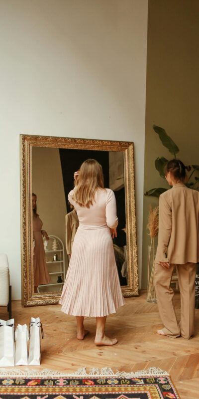 Two women trying on fashionable outfits in a boutique with large mirror.