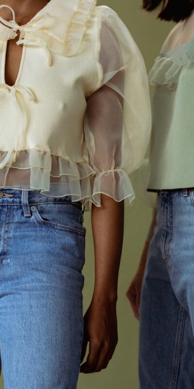 Two women wearing sheer blouses and denim jeans, embodying chic style.