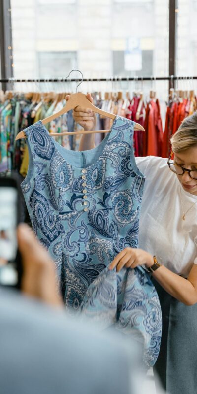 Woman inspecting a blue patterned dress in a retail clothing store. Fashion and shopping concept.